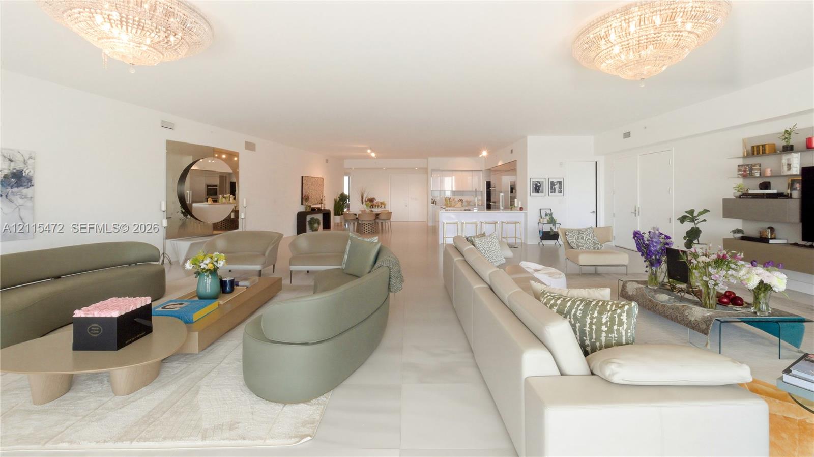 Open-concept interior featuring large-format tile flooring, dual crystal chandeliers, and built-in wall cabinetry