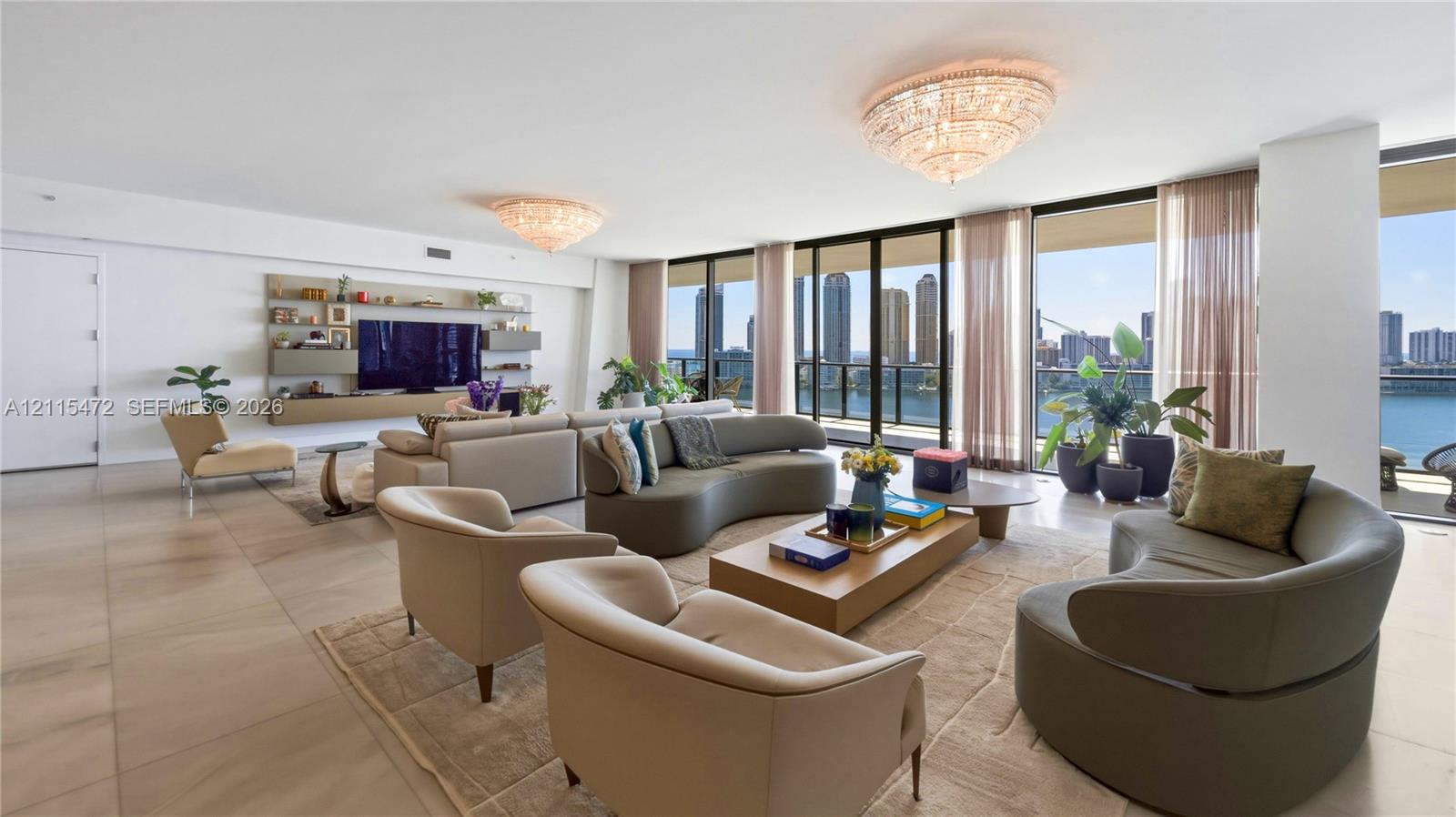 Open-concept living space featuring floor-to-ceiling windows, built-in wall cabinetry, dual crystal flush-mount chandeliers, and large-format tile flooring