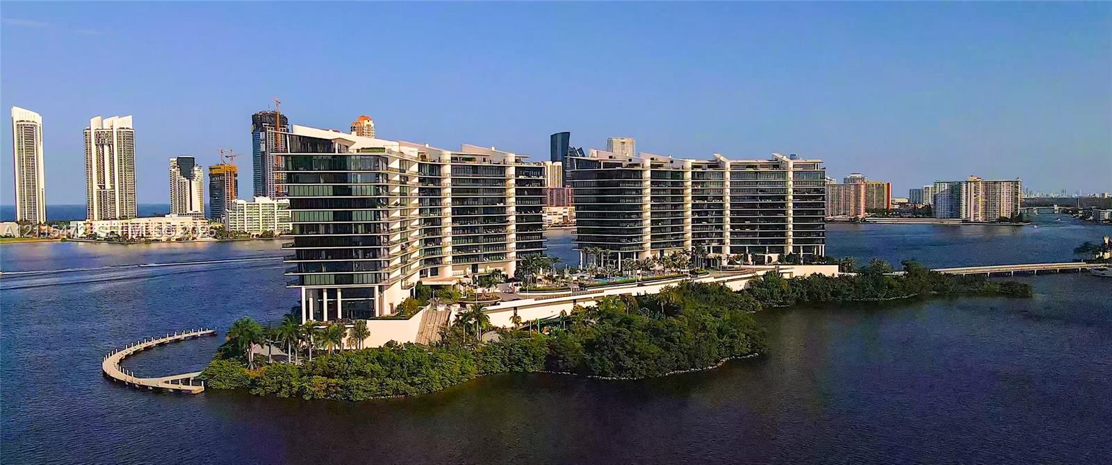Waterfront high-rise complex featuring expansive glass-walled balconies, ground-level swimming pools, and a private pedestrian pier on a coastal peninsula