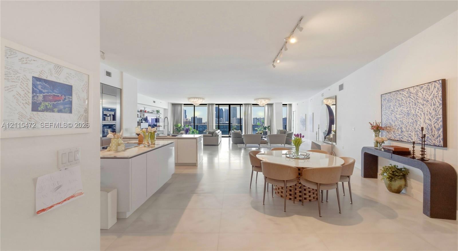 Open-concept floor plan featuring large-format tile flooring, kitchen island with stone countertop, track lighting, and floor-to-ceiling windows