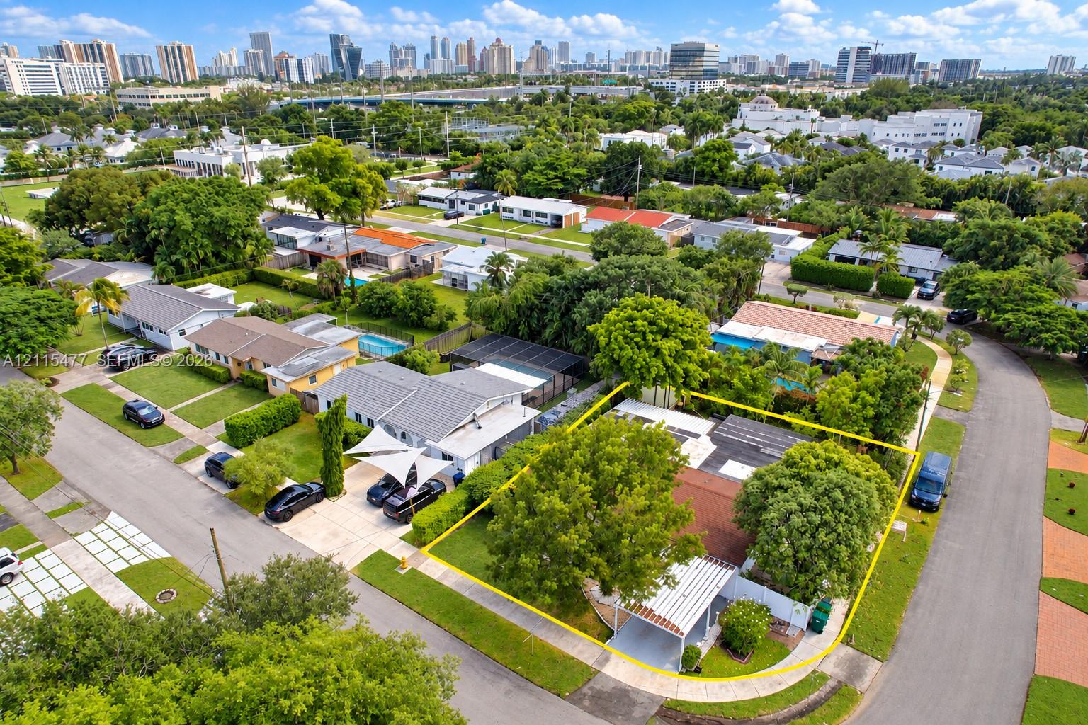 Aerial perspective featuring a corner lot property with a covered carport, mature shade trees, and perimeter fencing