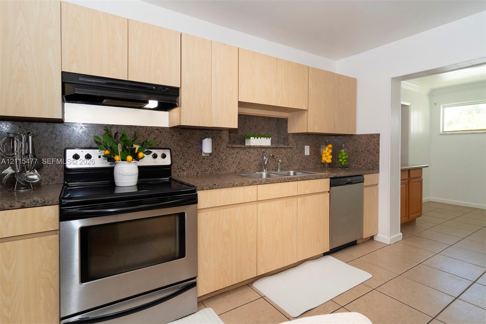 Kitchen featuring flat-panel wood cabinetry, speckled stone-finish countertops, stainless steel range with overhead hood, stainless steel dishwasher, and ceramic tile flooring