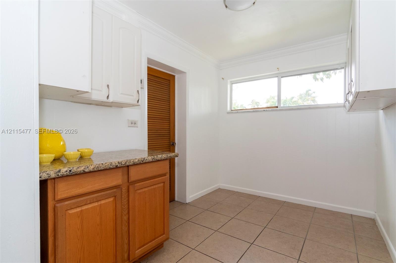 Kitchen area featuring light-toned cabinetry, stone-finish countertops, horizontal window, tile flooring, and louvered wood-finish door