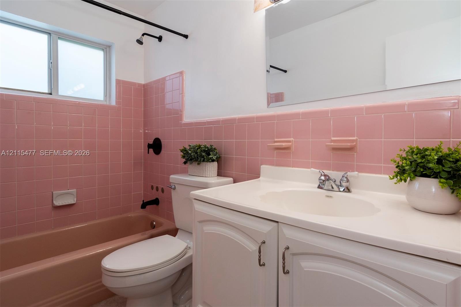 Bathroom featuring pink tile wall surround, integrated bathtub, white vanity with molded countertop, chrome dual-handle faucet, and black matte shower fixtures