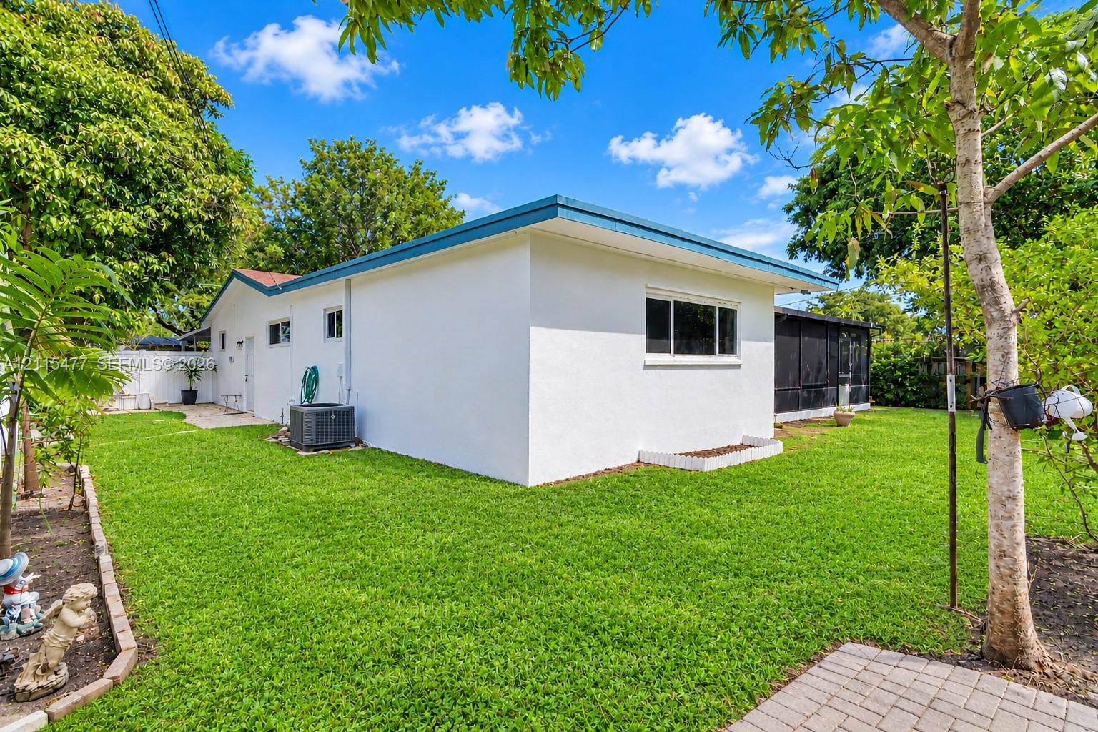 Exterior of the home featuring a white stucco facade, flat roofline, integrated screened-in enclosure, and expansive lawn with stone paver hardscaping
