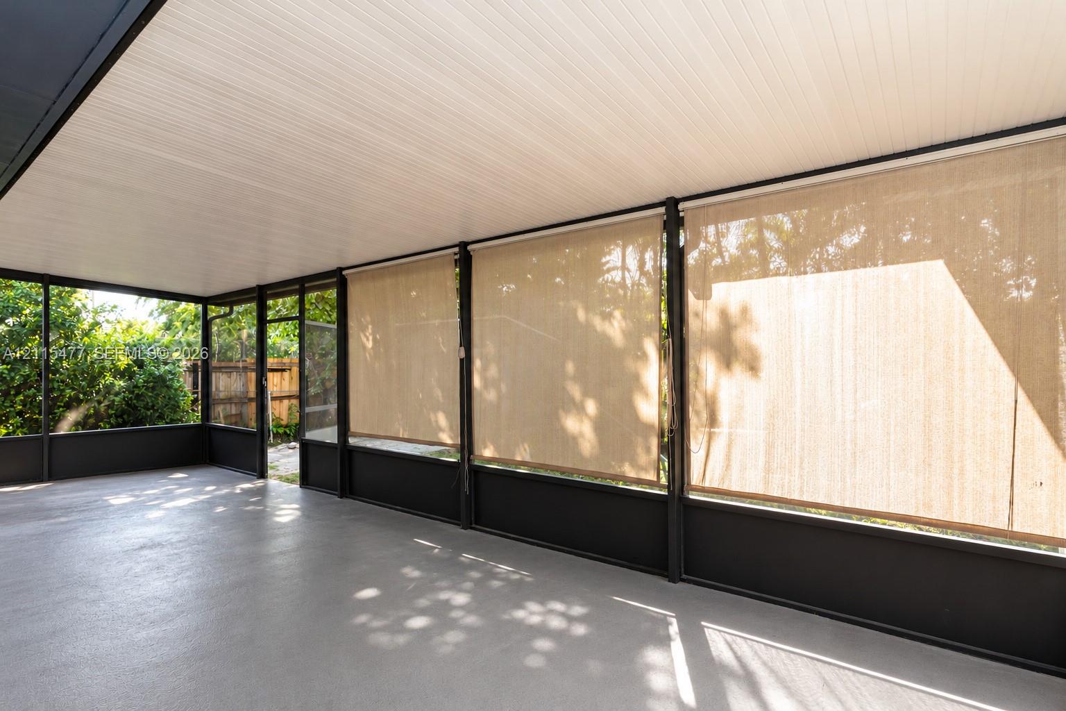 Screened-in porch featuring a solid roof, neutral concrete flooring, dark metal framework, and retractable sun shades
