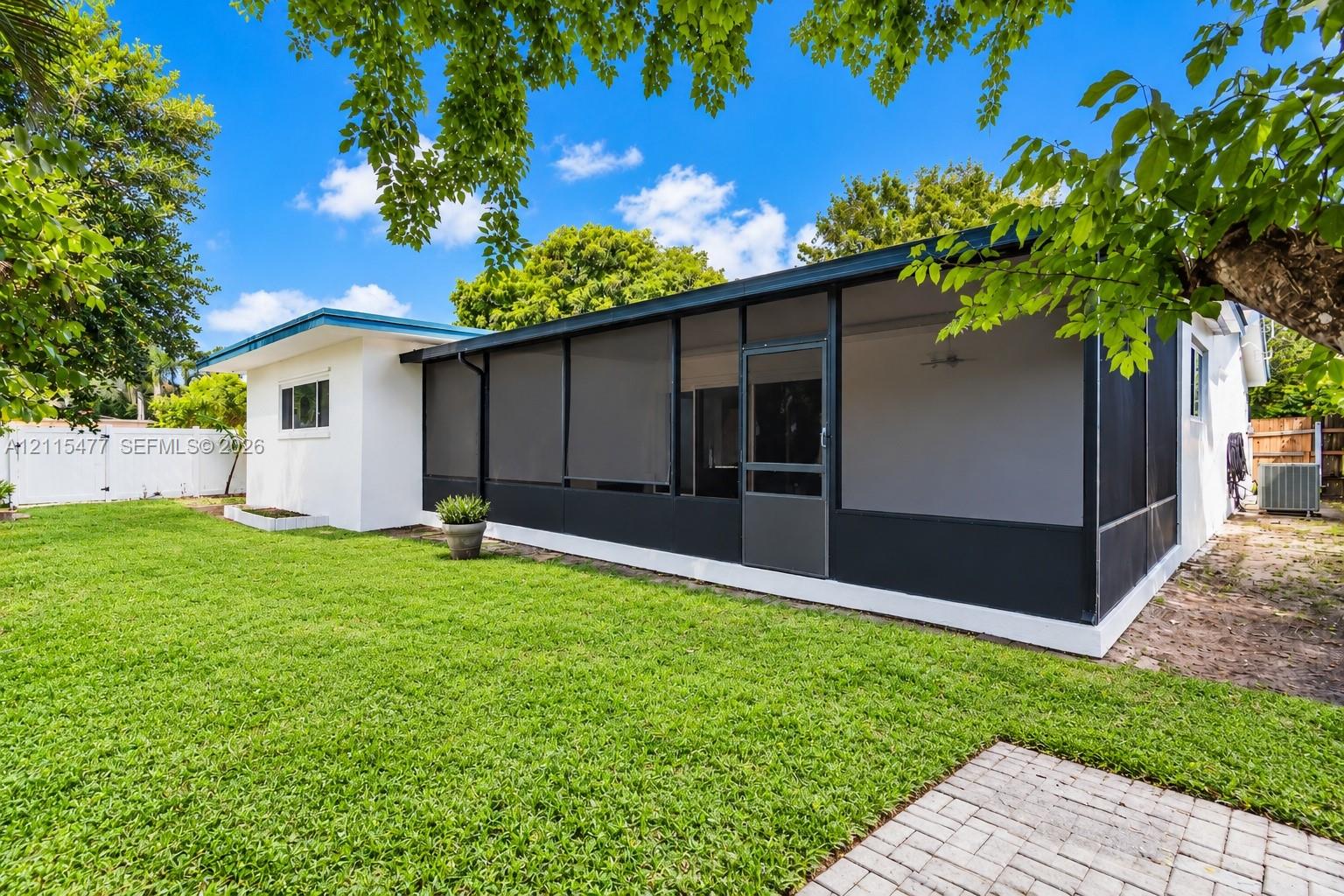 Backyard featuring a screened-in lanai, manicured lawn, paver patio, and white perimeter fencing