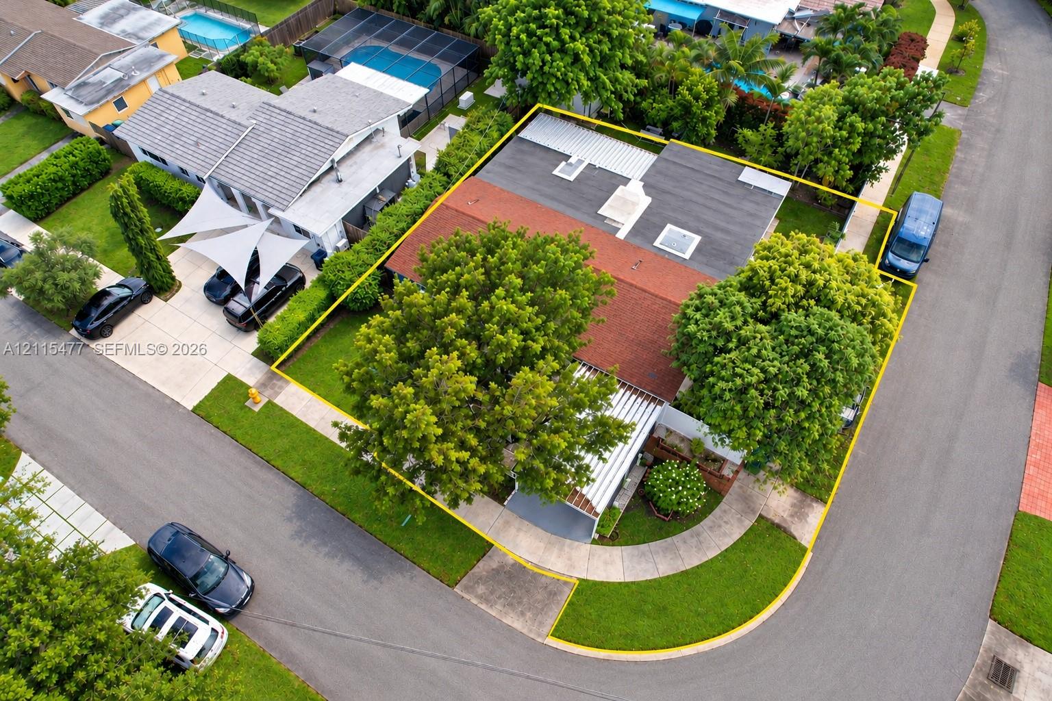 Corner lot featuring a multi-section roofline with skylights, a paved driveway, and mature landscaping