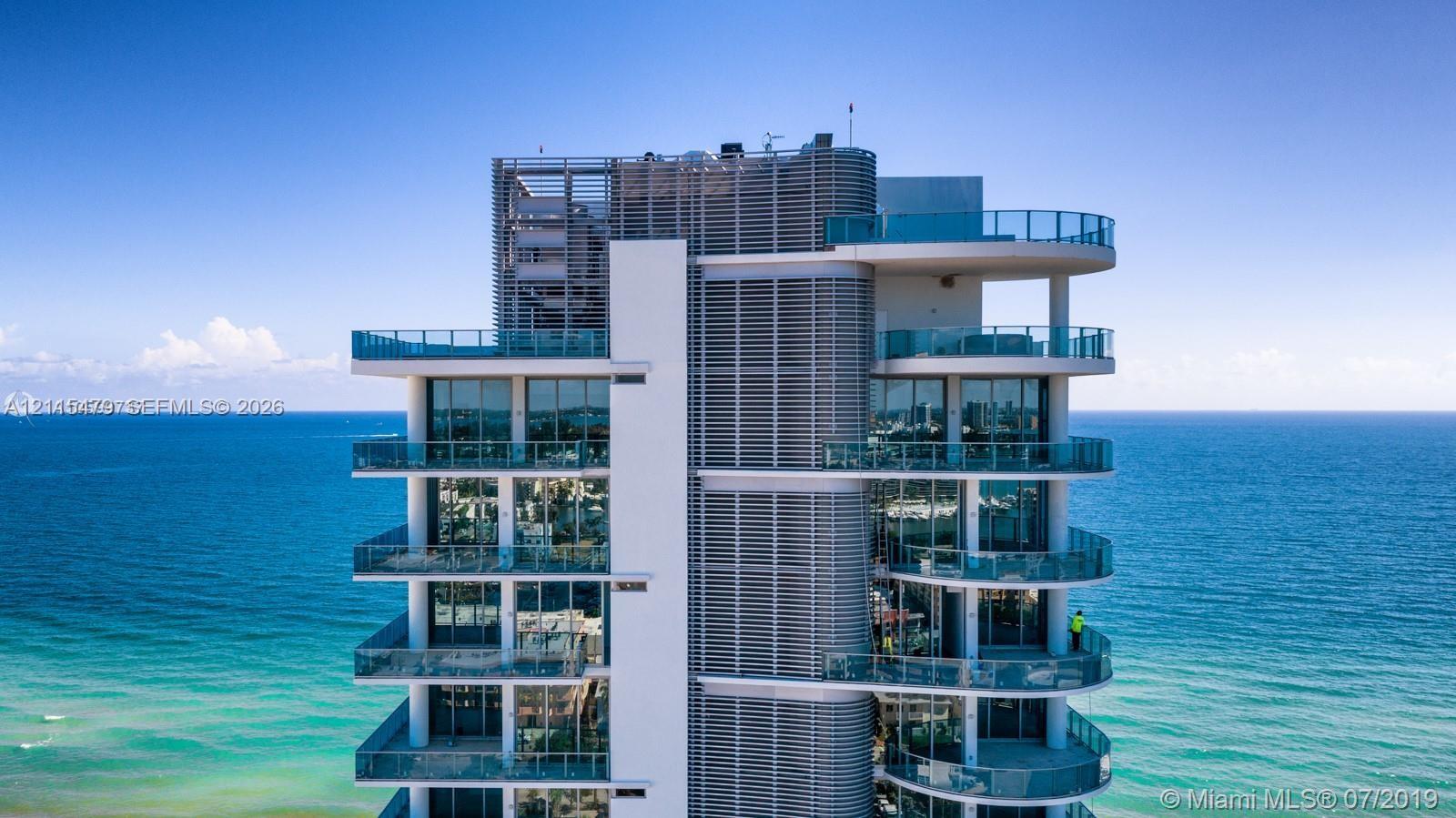 High-rise exterior featuring floor-to-ceiling glass windows, wraparound balconies, glass balustrades, and vertical louvered architectural screening