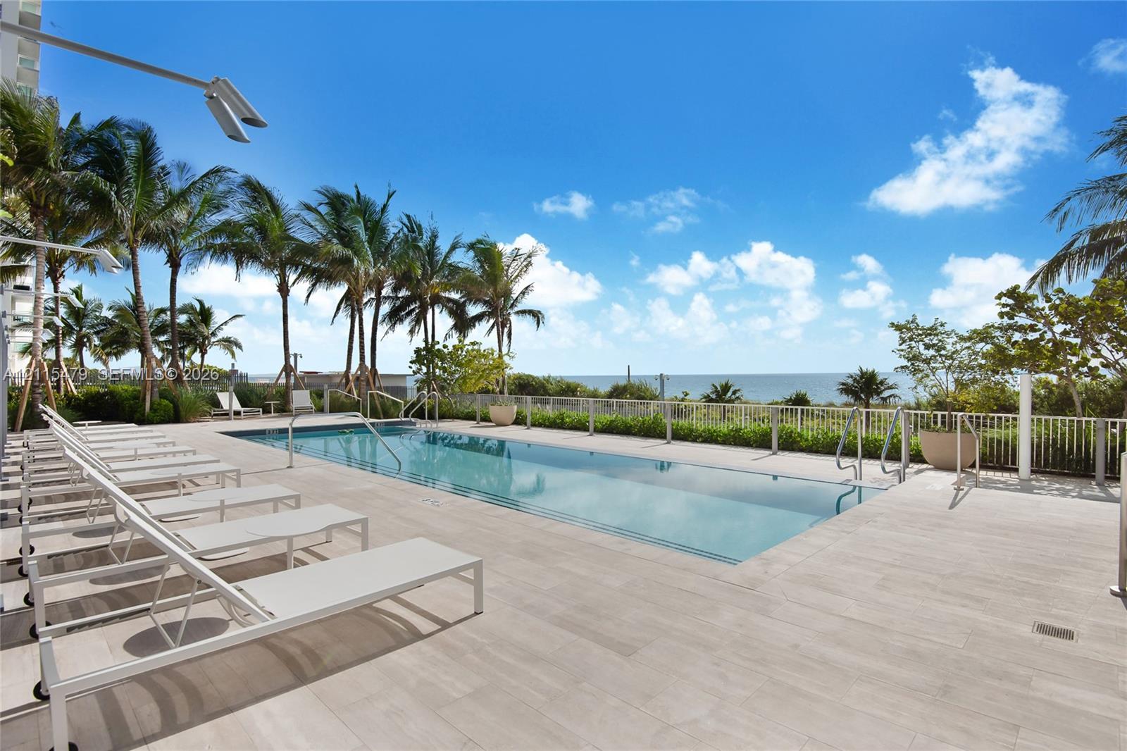 Rectangular swimming pool featuring a light-toned tile deck, metal pool ladders, and a minimalist perimeter railing
