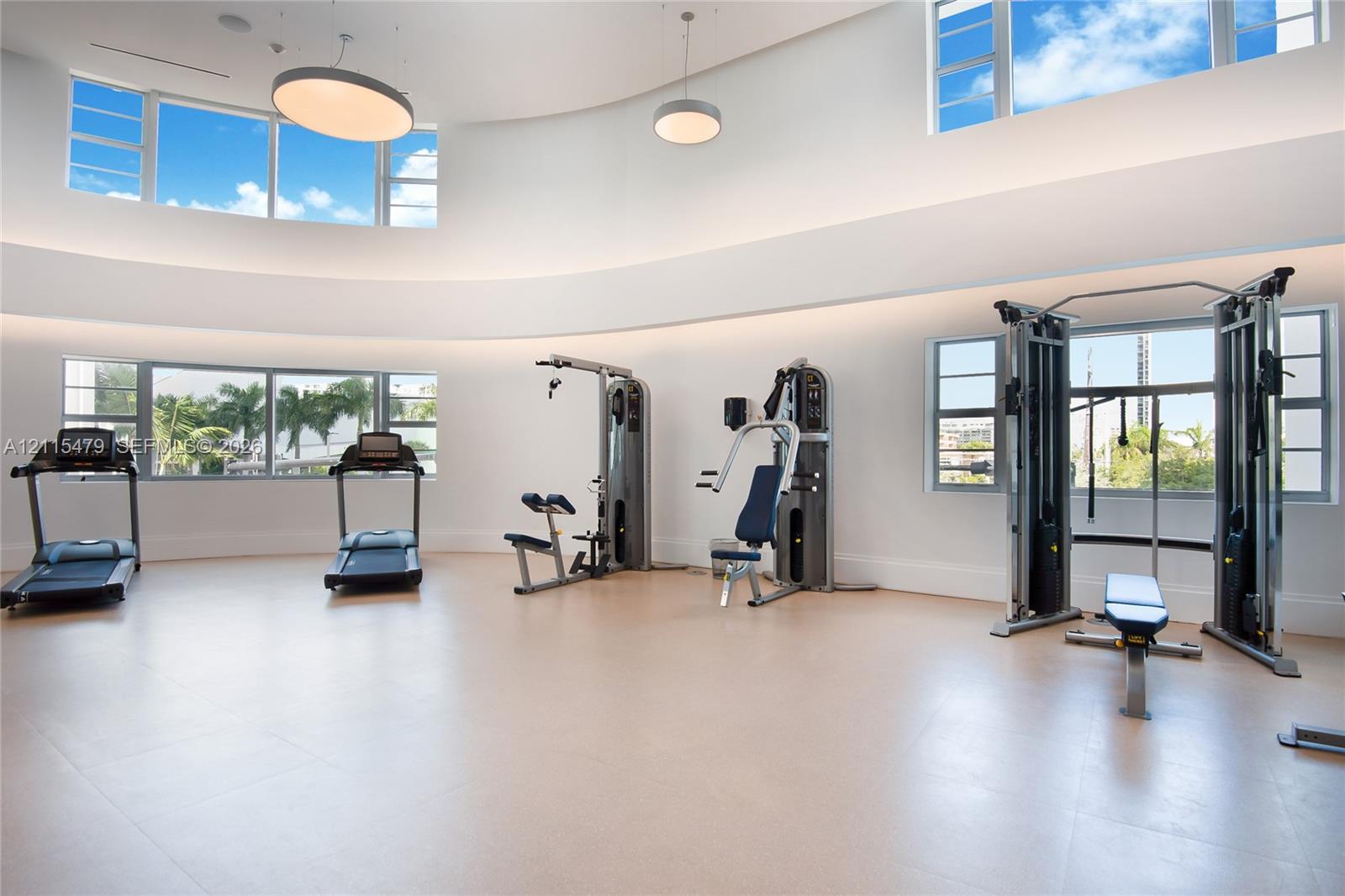 Expansive fitness area featuring soaring curved ceilings, multi-level oversized windows, recessed perimeter lighting, and neutral large-format tile flooring
