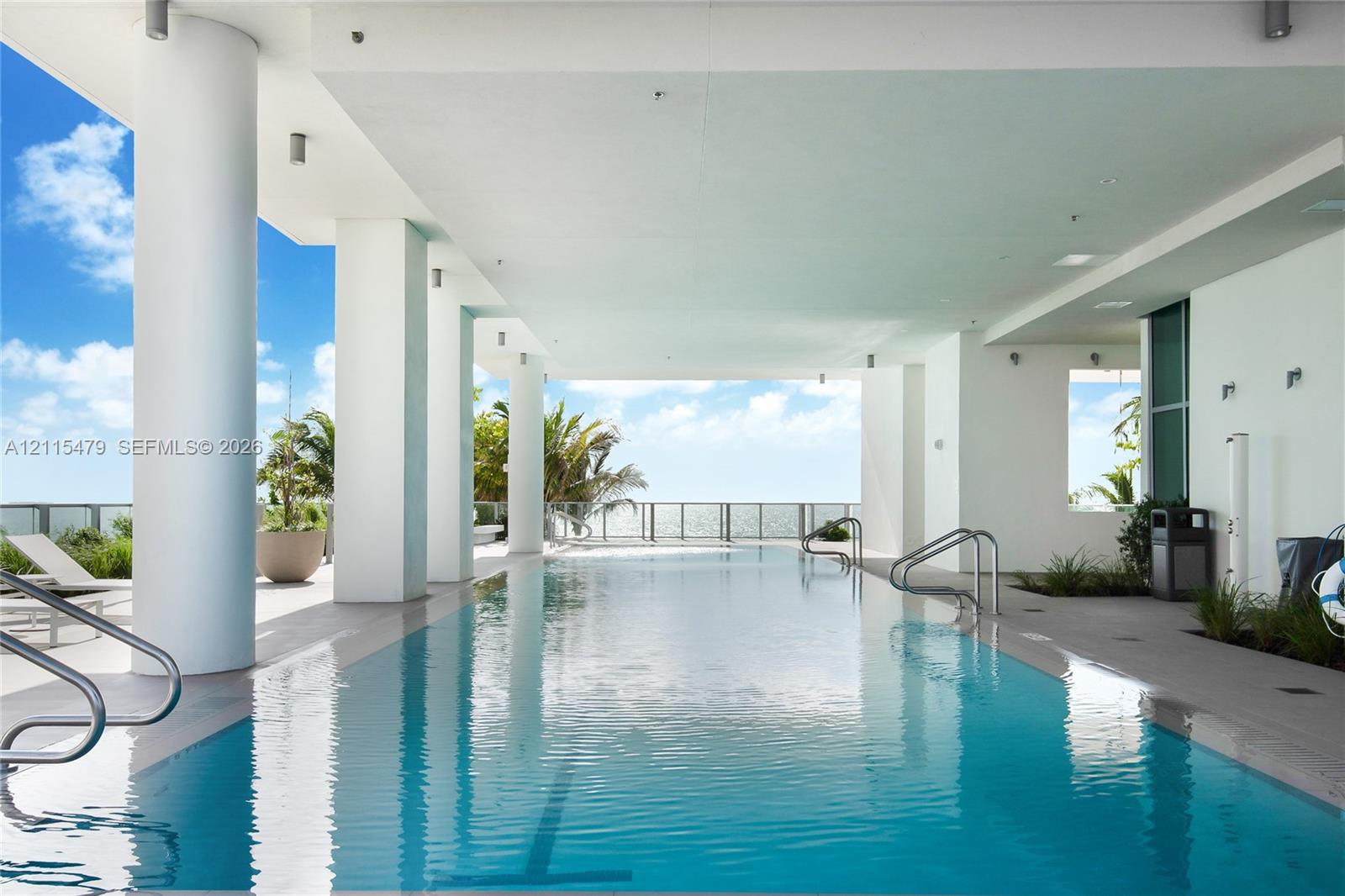 Covered lap pool featuring structural concrete pillars, stainless steel handrails, recessed ceiling lighting, and tile decking Covered lap pool featuring structural concrete pillars, stainless steel handrails, recessed ceiling lighting, and tile decking
