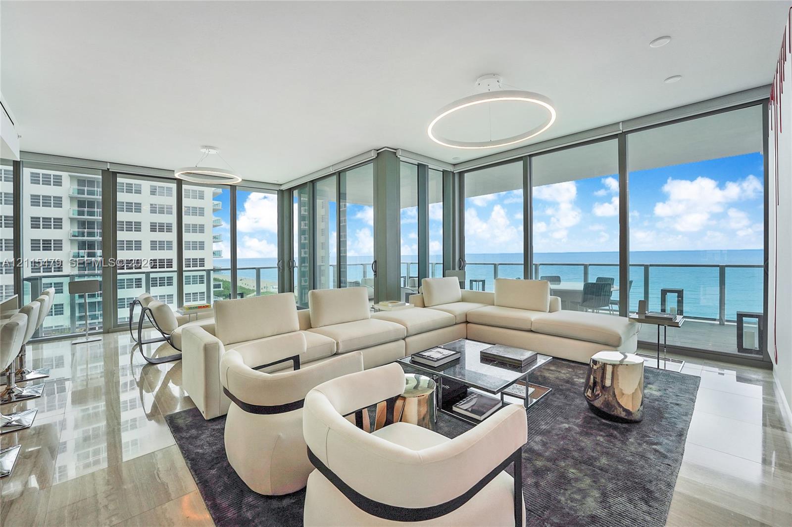 Floor-to-ceiling glass windows, polished tile flooring, circular pendant lighting, and an expansive balcony featuring a glass railing and ocean scenery Floor-to-ceiling glass windows, polished tile flooring, circular pendant lighting, and an expansive balcony featuring a glass railing and ocean scenery