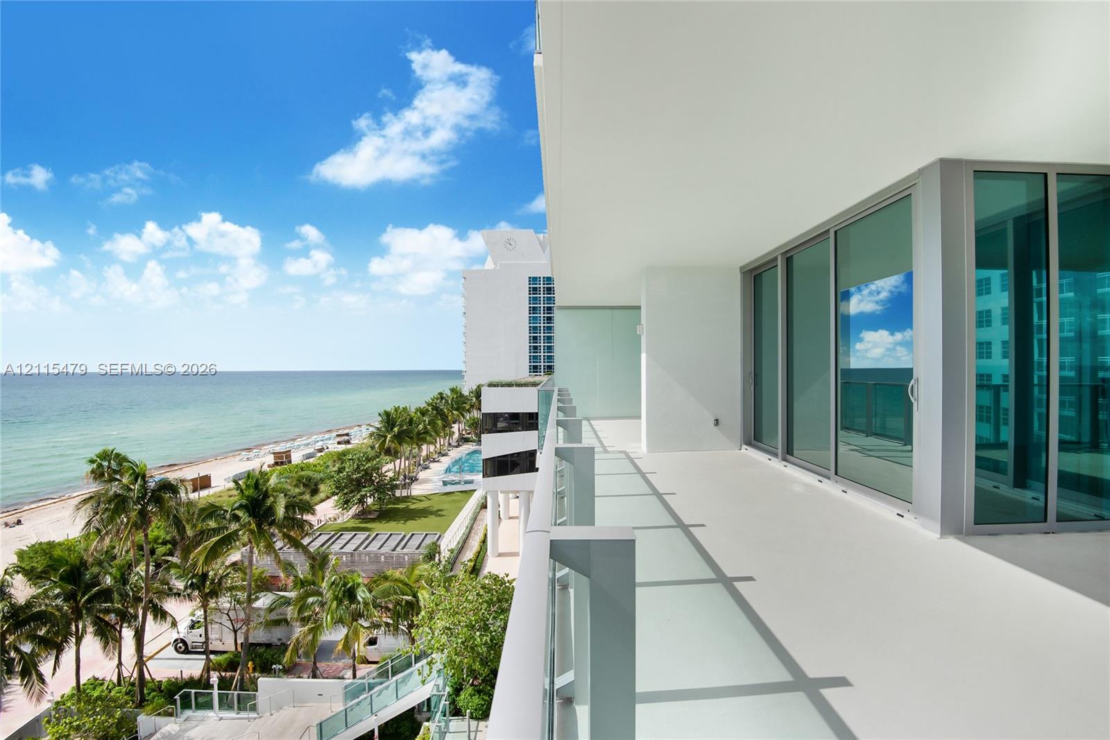 Covered balcony with a glass panel railing, expansive floor-to-ceiling glass sliding doors, and direct exposure to coastal scenery
