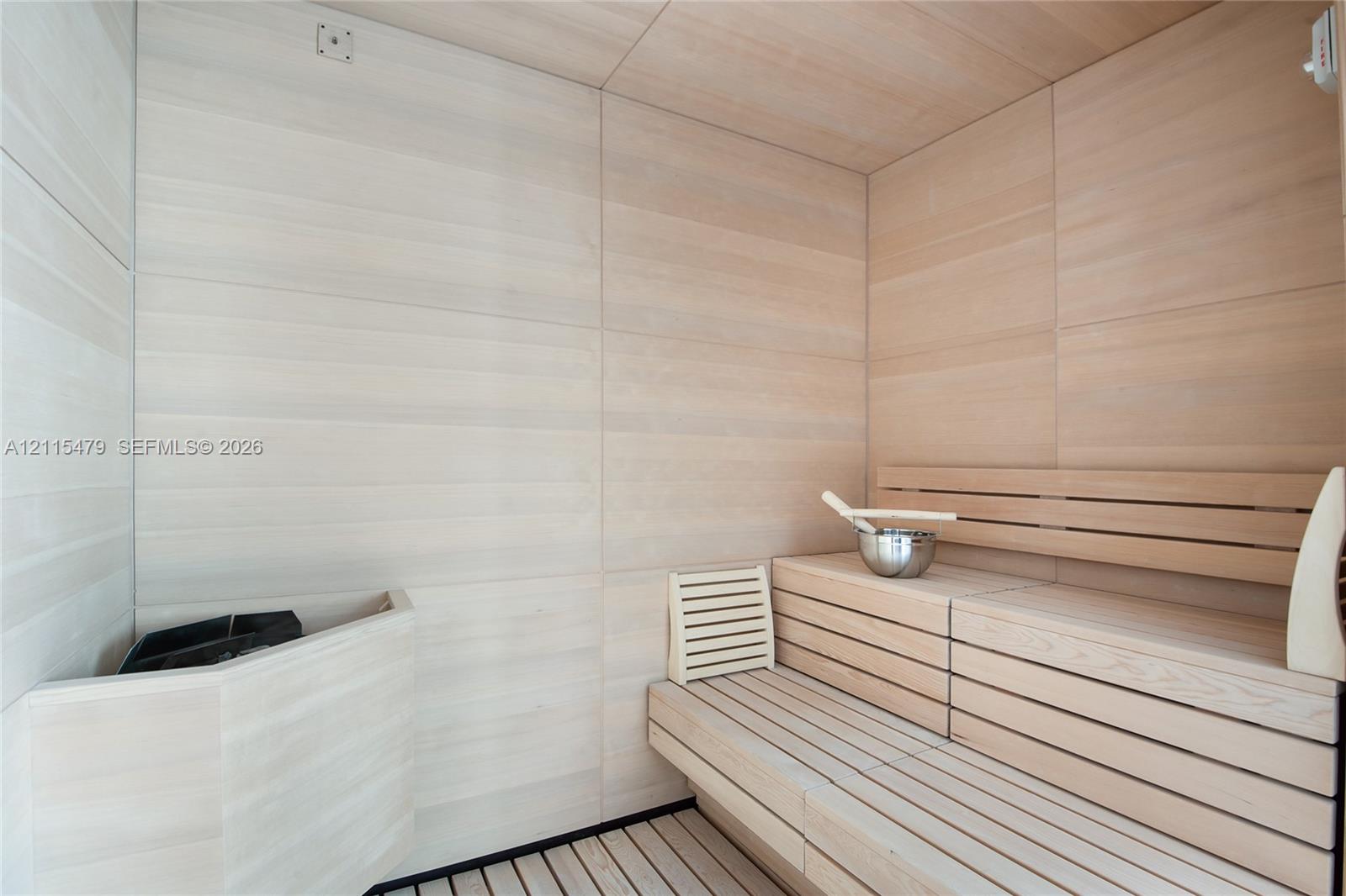 Sauna featuring light-toned wood wall paneling, tiered slatted wood bench seating, and a corner-mounted heater unit