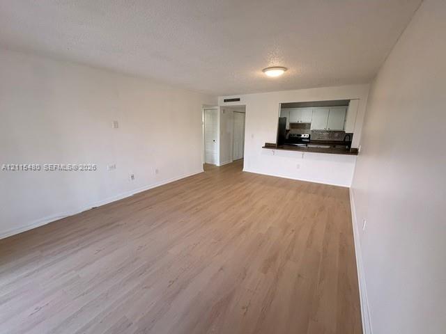 Open-concept interior featuring light wood-finish flooring, a pass-through kitchen opening, flush-mount ceiling lighting, and solid-core interior doors