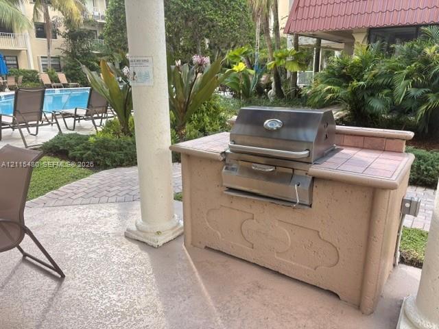 Outdoor kitchen station with a stainless steel built-in grill and tile-surround countertop, situated on a textured concrete patio with decorative column support
