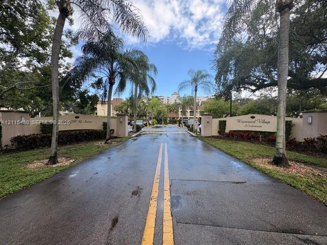 Gated community entrance featuring dual stucco monument signage, palm tree landscaping, and paved driveway