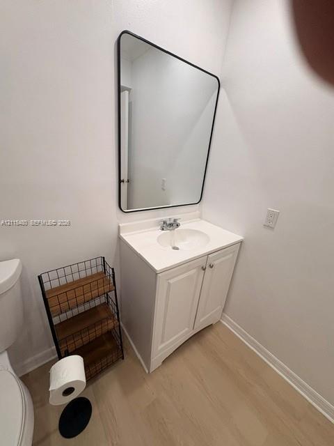White vanity cabinet with an integrated white countertop, rounded sink basin, black-framed wall mirror, and light wood-finish flooring