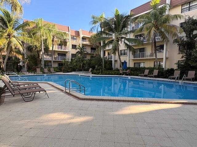 Community swimming pool featuring a paved deck, metal railings, and perimeter palm trees