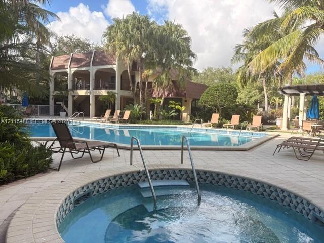 In-ground swimming pool and circular spa featuring tile accents, surrounded by a paved deck and mature palm trees