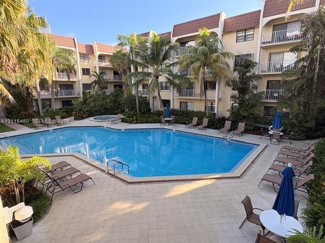 Community swimming pool and hot tub set within a paver-stone deck, surrounded by mature palm trees and multi-story residential building with private balconies