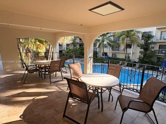 Covered balcony featuring tile flooring, arched architectural supports, and decorative metal railings overlooking a swimming pool