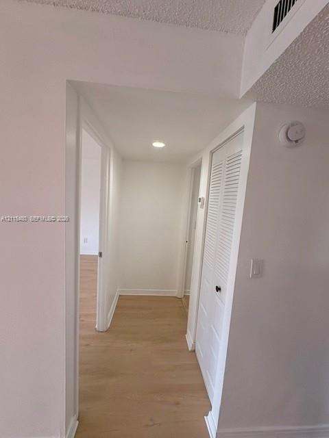 Hallway featuring wood-finish flooring, recessed lighting, and white louvered closet doors