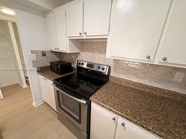 Kitchen featuring white cabinetry, stone-finish countertops, subway-style tiled backsplash, stainless steel electric range, and pantry storage