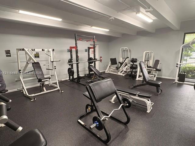 Fitness area featuring rubberized flooring, exposed ceiling beams, and industrial-grade overhead lighting