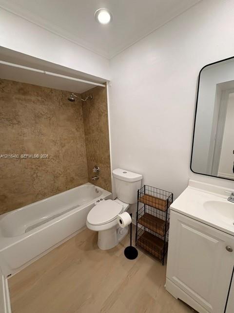 Bathroom featuring a white vanity cabinet with an integrated sink, wall-mounted rectangular mirror with a black frame, wood-finish flooring, and a bathtub surround with textured tile detailing