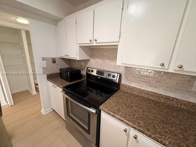 Kitchen featuring white cabinetry, stone-finish countertops, subway tile backsplash, stainless steel electric range, and an integrated pantry with wire shelving