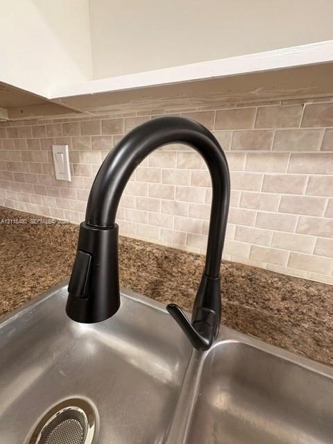 Matte black high-arc pull-down faucet, dual-basin stainless steel sink, stone-composite countertop, and brick-pattern tile backsplash
