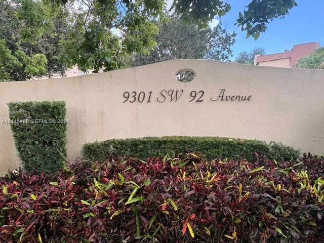Stucco monument signage featuring dimensional house numbers and an oval architectural accent, surrounded by manicured shrubs and ornamental foliage