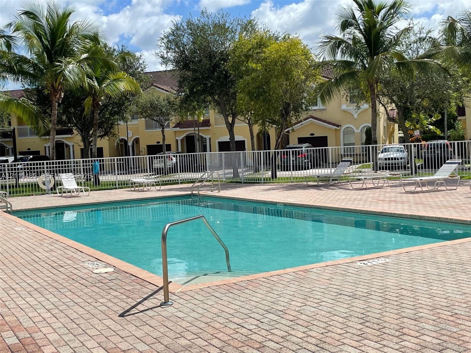 Swimming pool featuring a brick-paver deck, metal perimeter fencing, and stainless steel handrails