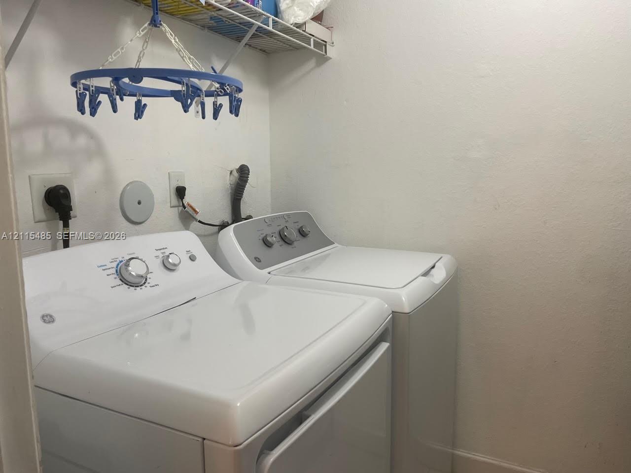 Laundry area featuring white washer and dryer units with integrated dial controls and overhead wire shelving