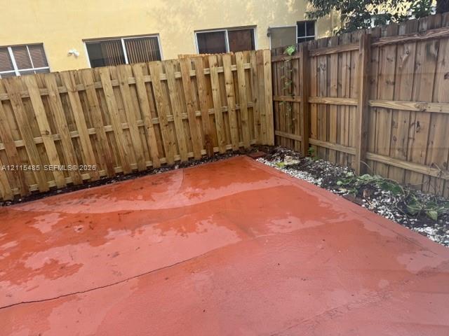 Rear courtyard featuring a terra-cotta finished concrete patio, enclosed by a full-height wood picket fence with integrated gravel landscaping beds