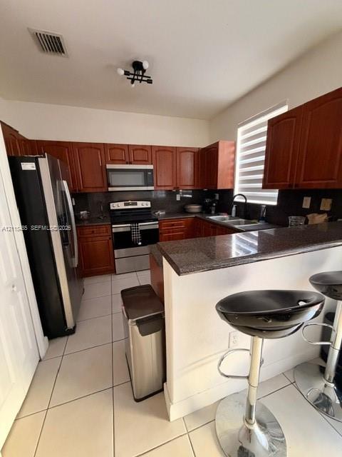 Kitchen featuring wood cabinetry, stone-surface countertops, stainless steel appliances, ceramic tile flooring, and a breakfast bar