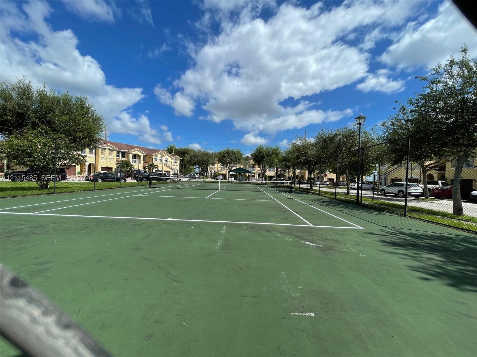 Hard-court tennis facility featuring a high-tension perimeter fence, painted court markings, and integrated post lighting