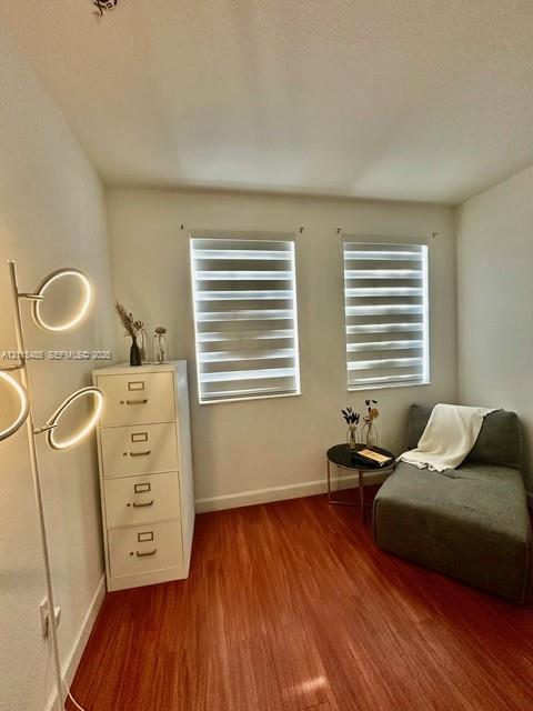 Room featuring wood-finish flooring, dual windows with banded roller shades, and neutral wall tones