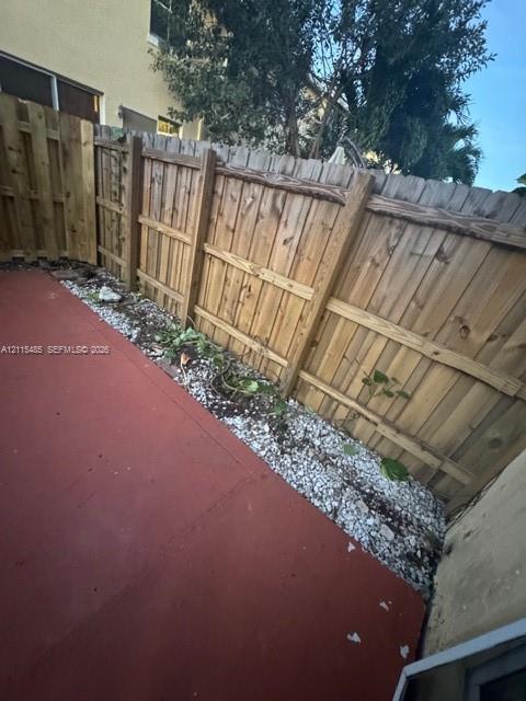 Private outdoor space featuring a red-toned concrete patio, bordered by decorative white gravel, and enclosed by a wood-plank privacy fence