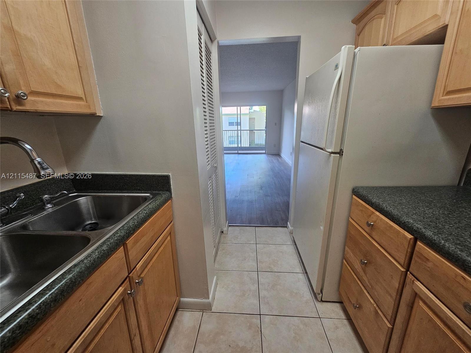 Kitchen featuring natural wood cabinetry, stone-finish countertops, a double-basin stainless steel sink, tiled flooring, and a louvered pantry door