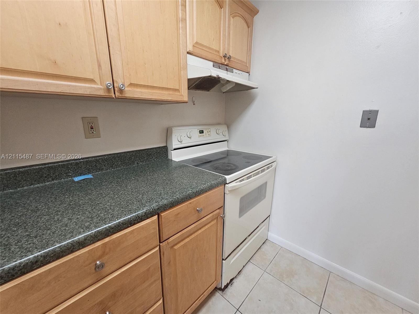 Kitchen featuring light wood-finish cabinetry, solid-surface countertops, built-in range, range hood, and tile flooring
