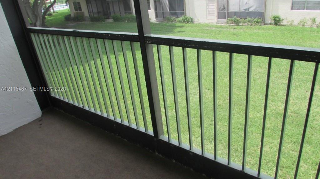Screen-enclosed balcony featuring a solid surface floor and a vertical metal railing overlooking a grass lawn