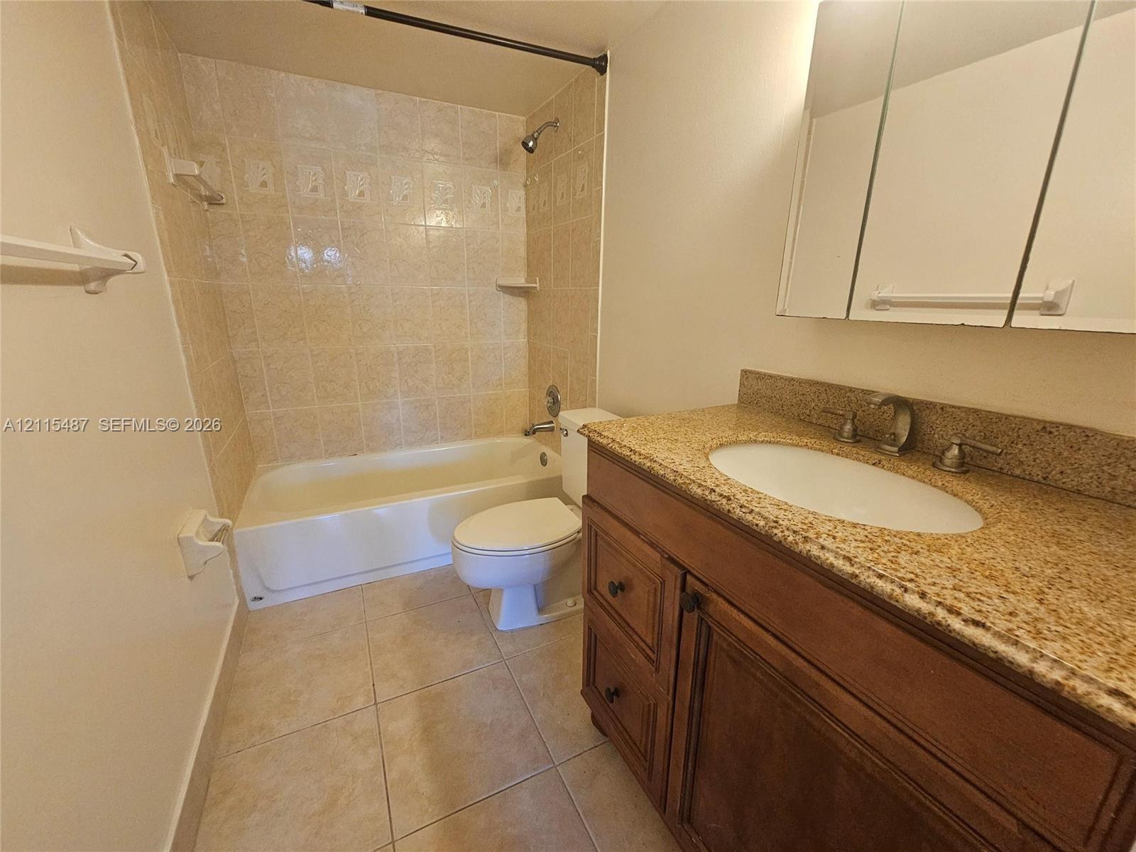 Bathroom featuring a wood vanity with stone-finish countertop, undermount sink, mirrored medicine cabinet, and a tiled tub-shower combination