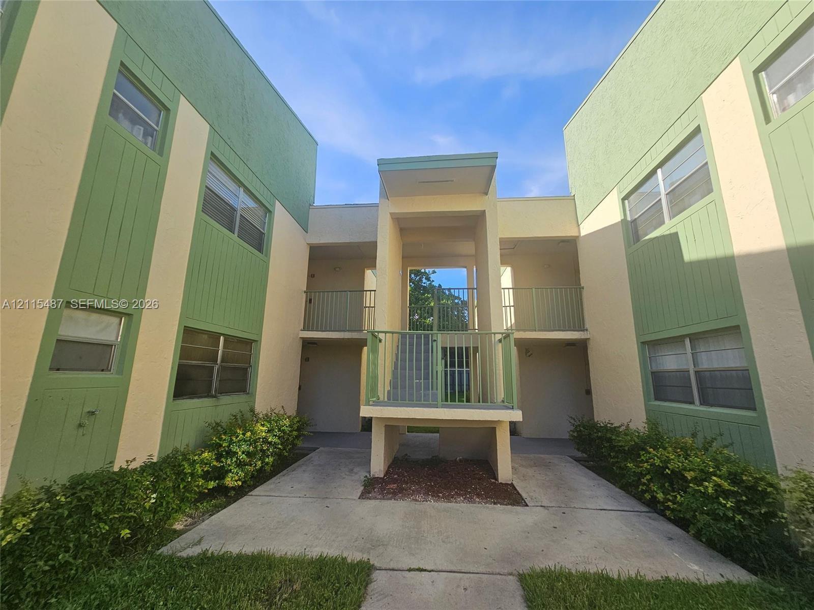 Two-story exterior featuring a stucco and vertical siding facade, metal railings, recessed entrances, and concrete walkways