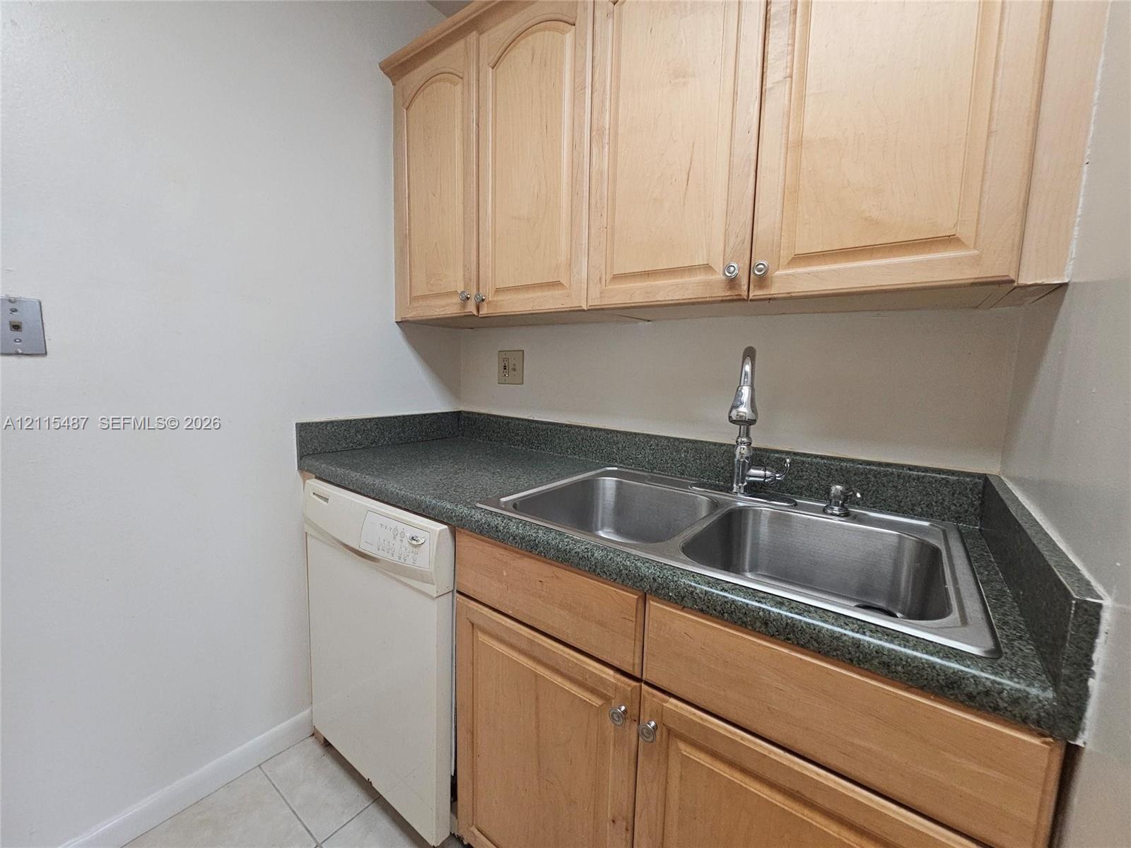 Light-wood cabinetry, dark stone-finish countertops, dual-basin stainless steel sink with high-arc faucet, and integrated dishwasher
