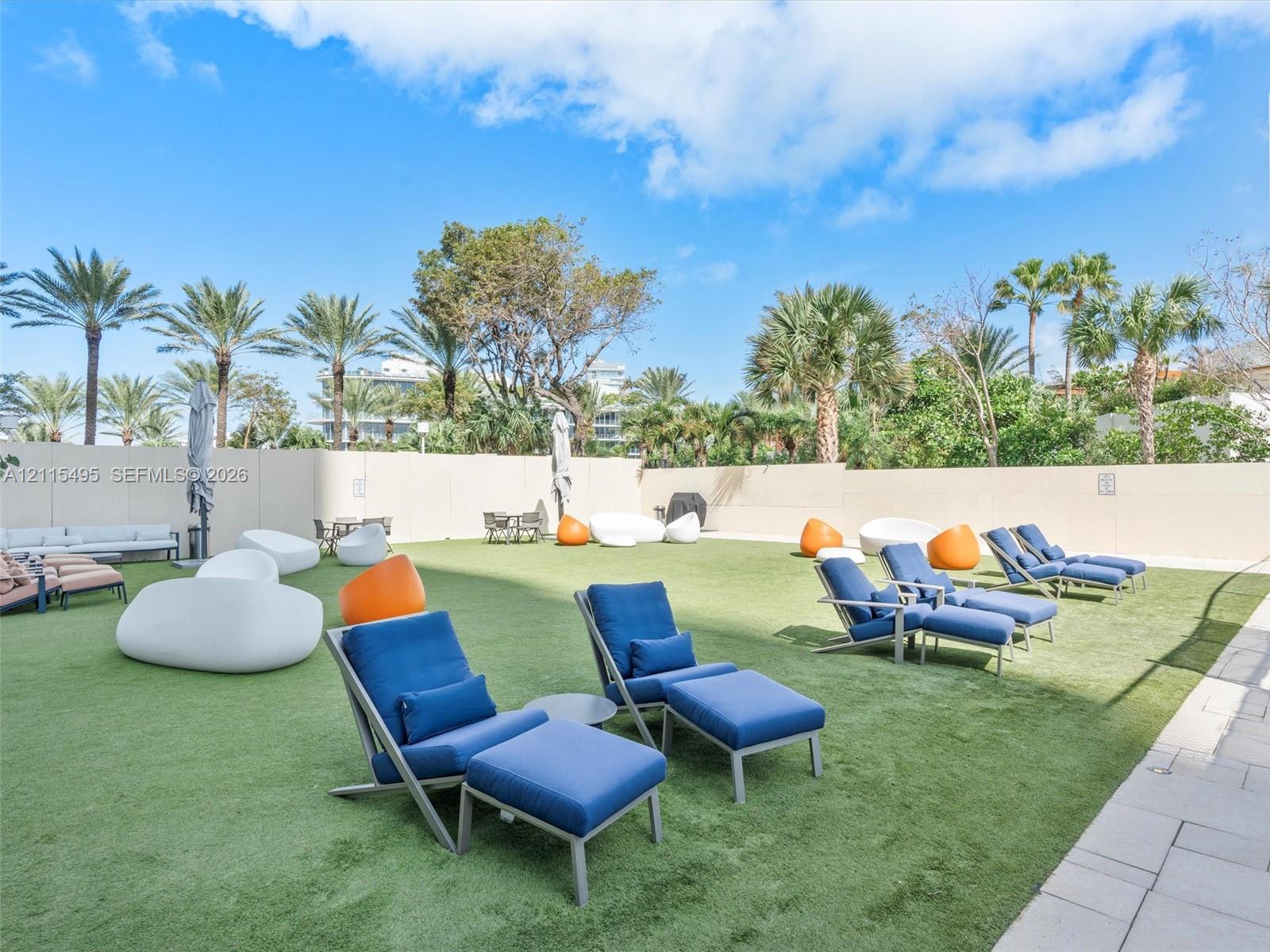 Expansive outdoor recreation space featuring artificial turf, perimeter concrete walls, and mature palm trees
