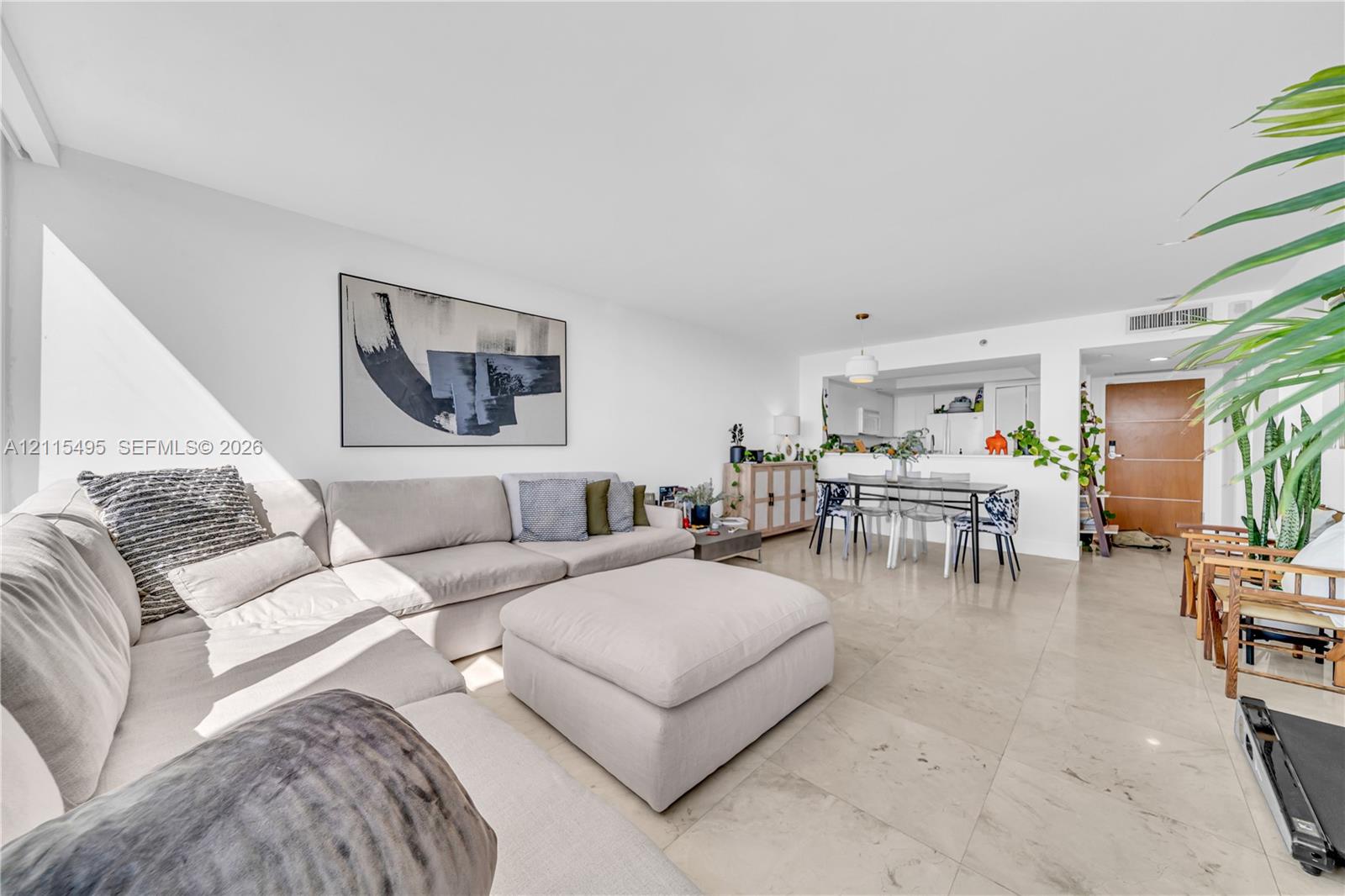 Open-concept interior featuring large-format stone flooring, a pass-through kitchen opening, recessed lighting, and a solid-core wood entry door