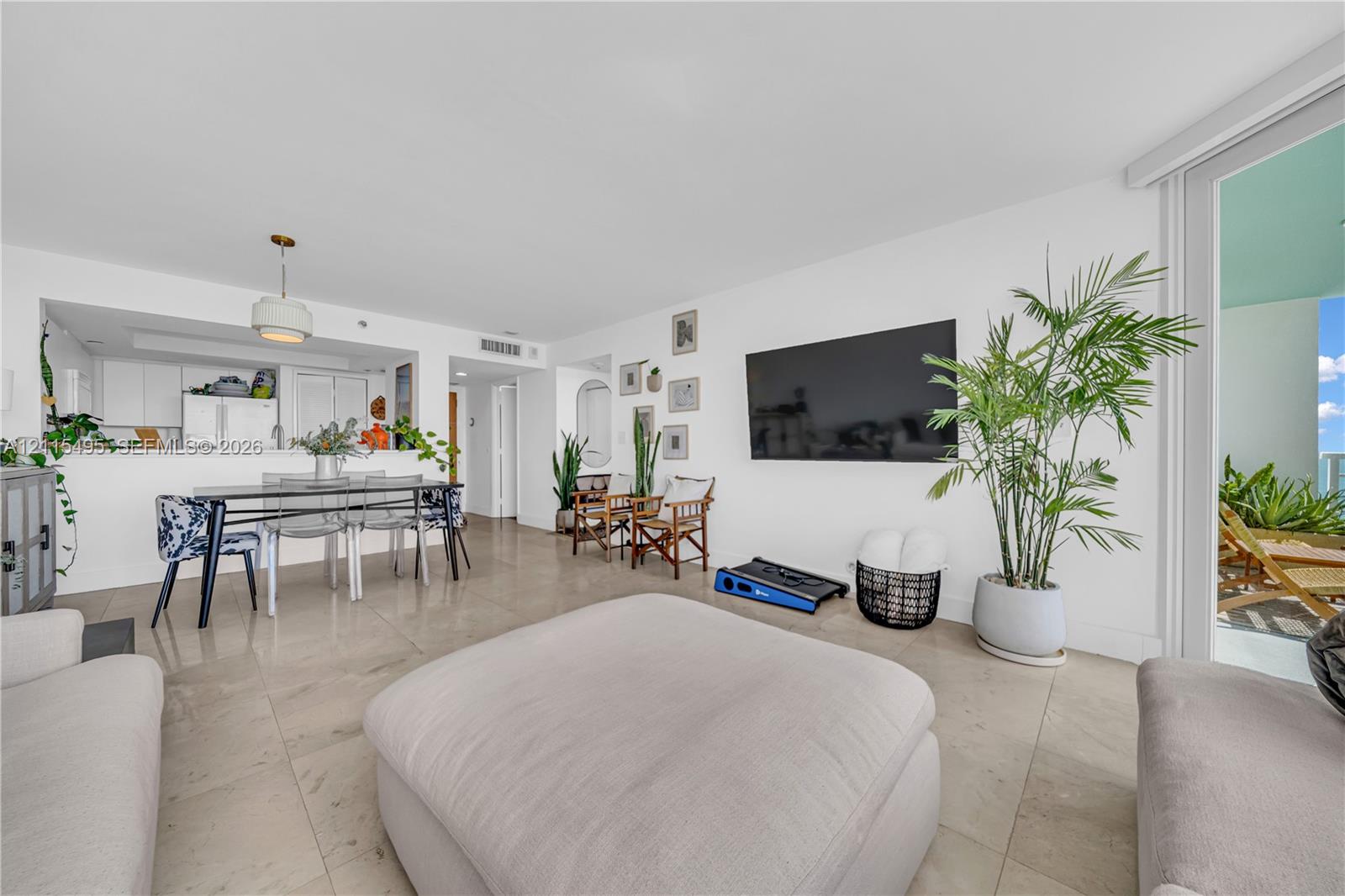 Open-concept floor plan with neutral stone-finish tile flooring, recessed ceiling lighting, a pass-through kitchen window, and sliding glass doors providing outdoor access